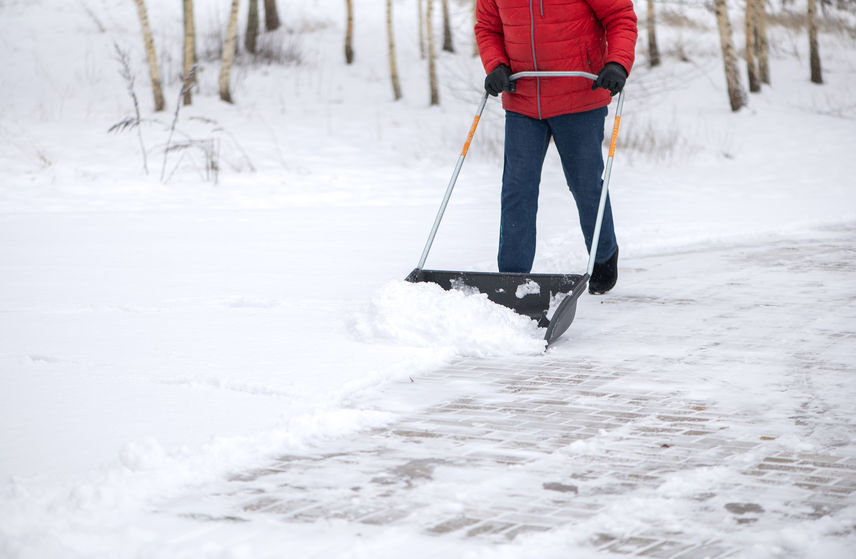 Man with a snow shovel clears tenants’ driveway in front of apartment complex