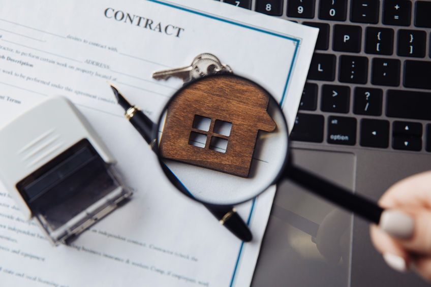 Wooden house, magnifying glass and rental contract on a laptop