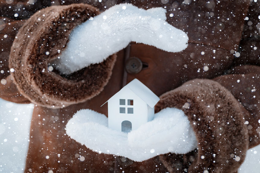 Small model of a house in wool gloves on the street in winter against the background of snow